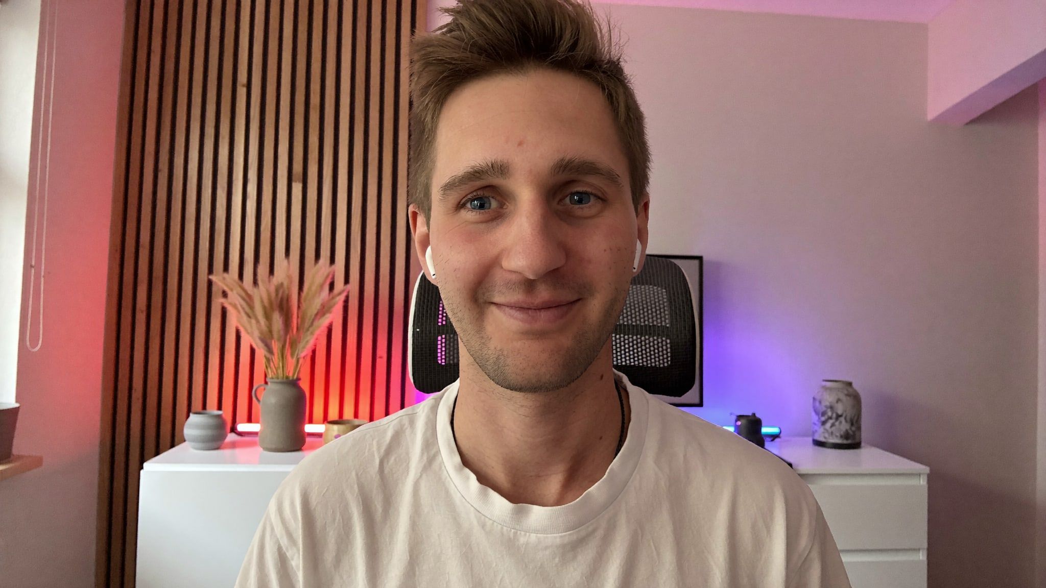 Kevin Baum im Videocall an seinem Schreibtisch, im Hintergrund eine Holzlattenwand mit farbigem Licht.