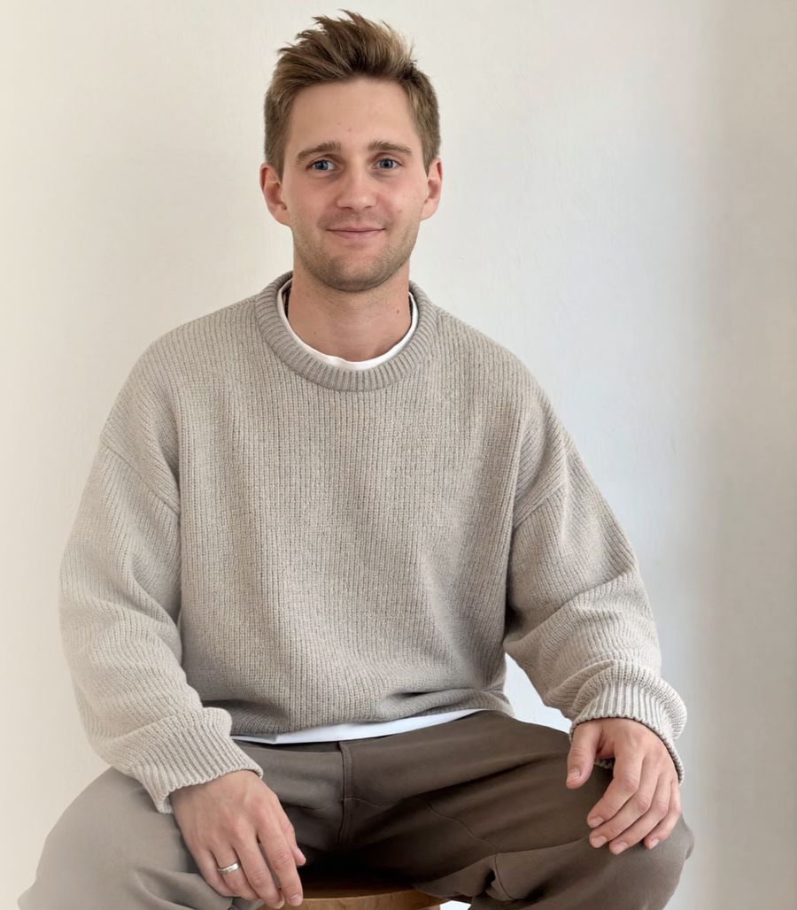 Kevin Baum auf einem Hocker vor heller Wand